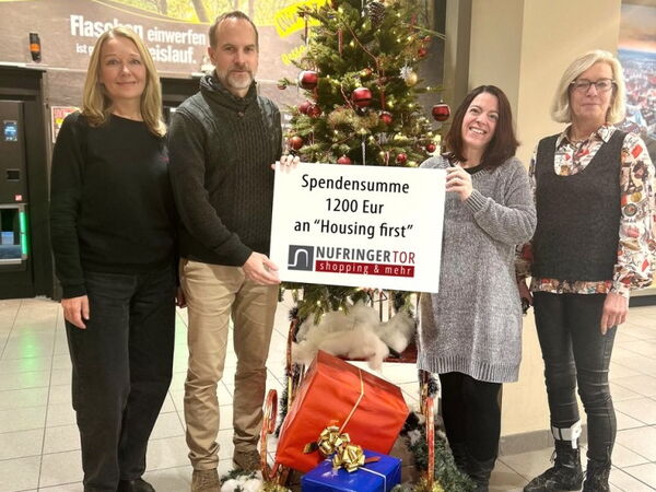 4 Personen stehen vor einem Weihnachtsbaum mit einem Plakat auf dem die Spendsumme 1200 Euro steht